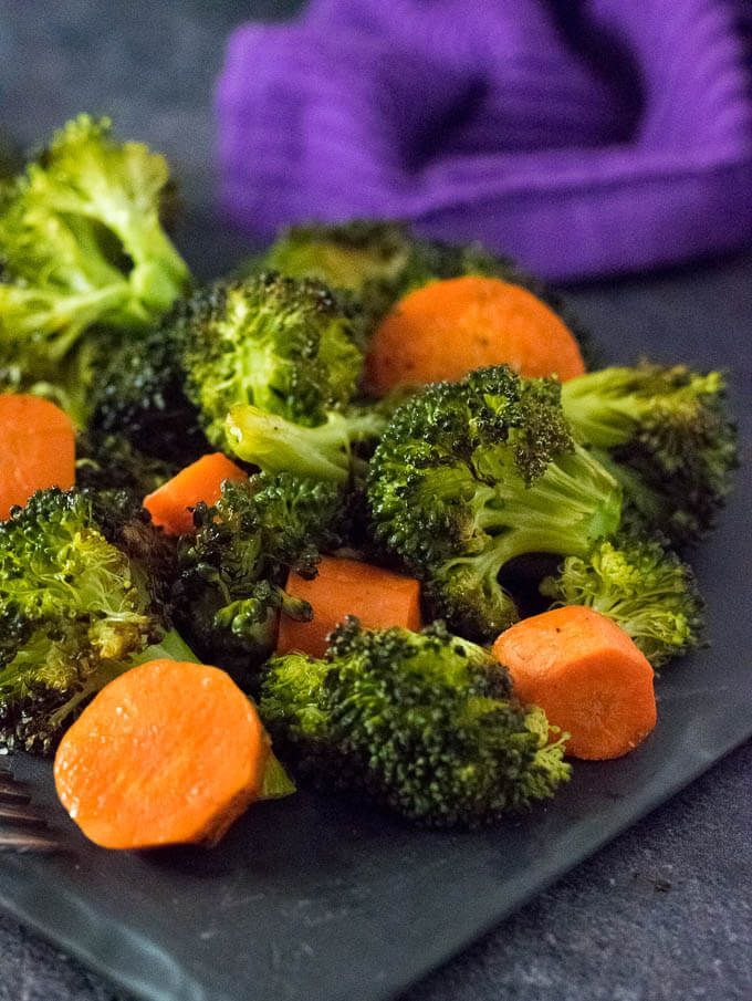 Roasted broccoli and carrots on a plate with purple cloth background. Healthy side dish, vibrant vegetables.