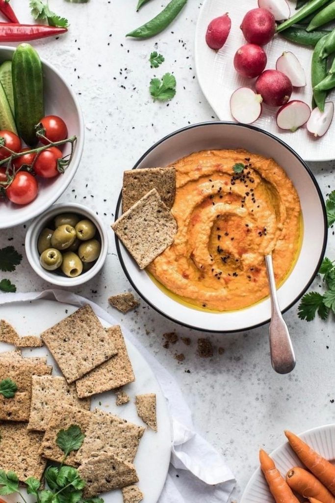 Creamy hummus with crackers and fresh veggies: tomatoes, radishes, peas, and olives, perfect for a healthy snack.