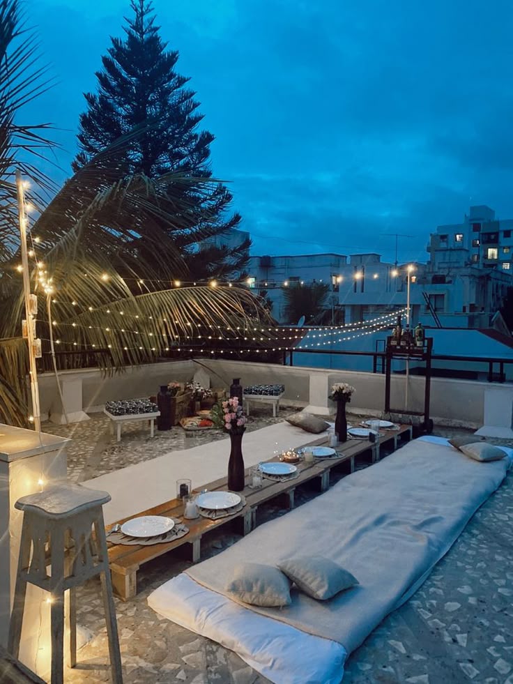 Cozy rooftop dinner setting with string lights, cushions, and a long table at dusk. Perfect for a romantic evening.