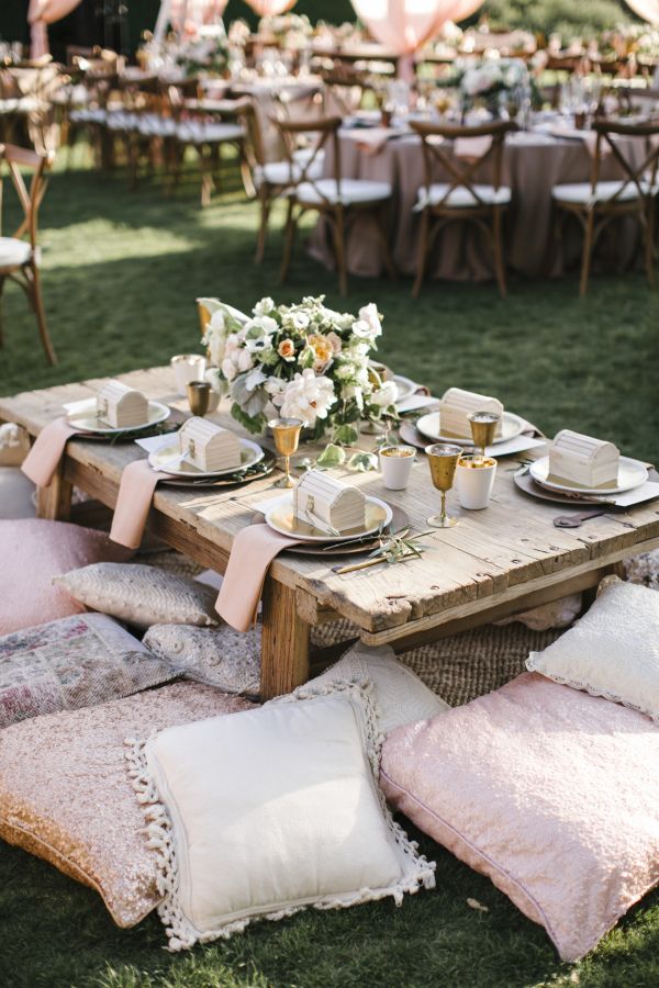 Outdoor boho picnic setting with low wooden table, floral decor, and cushions on grass for a stylish gathering.