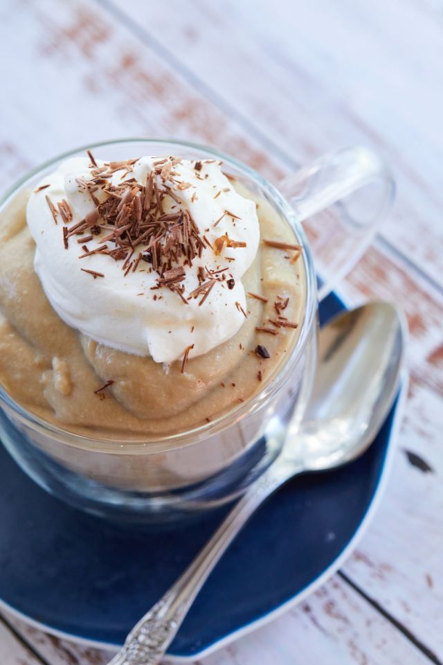 Creamy dessert in a glass cup topped with whipped cream and chocolate shavings, placed on a blue saucer with a spoon.