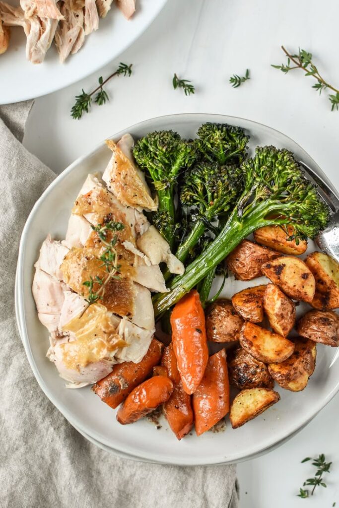 Roasted chicken with broccolini, carrots, and potatoes on a plate, garnished with fresh herbs.