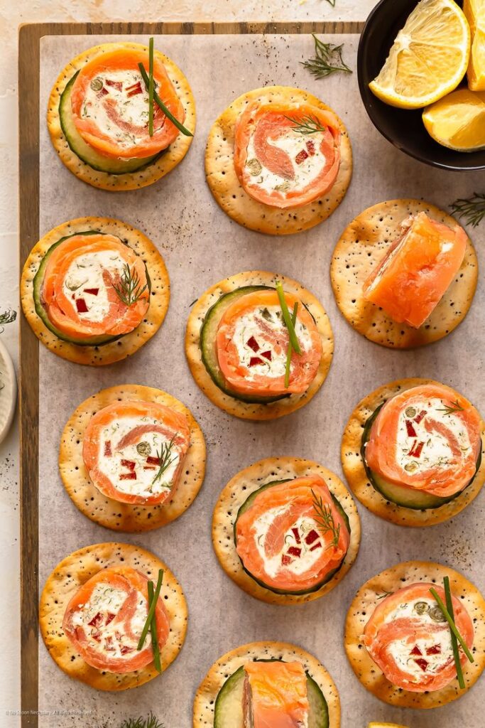 Smoked salmon and cream cheese canapés on crackers, garnished with dill and chives, served with lemon wedges.