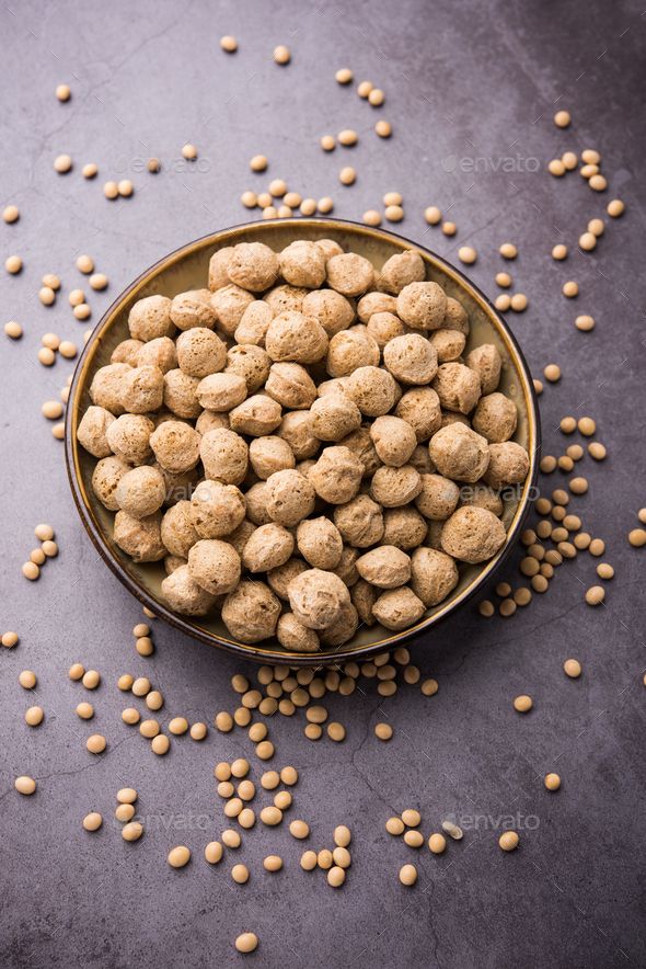 Bowl of textured soybean chunks with scattered soybeans on a dark surface, showcasing vegetarian protein source.