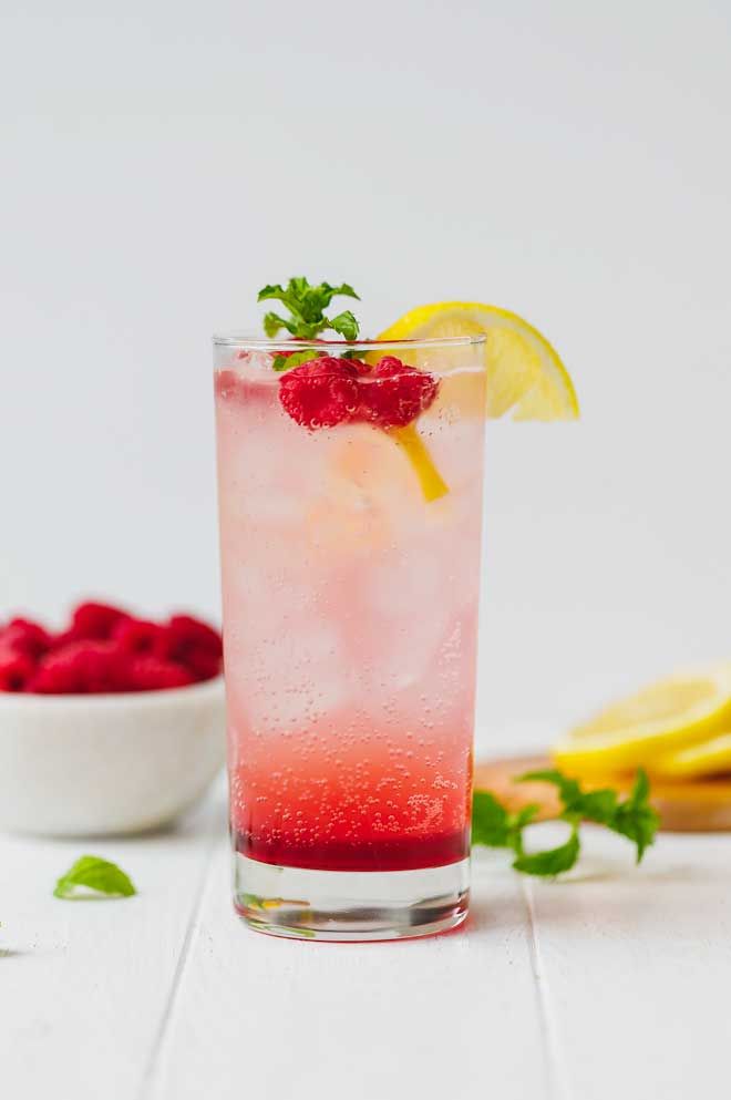 Refreshing raspberry lemonade garnished with mint and lemon slice in a tall glass, ideal for a summer drink.
