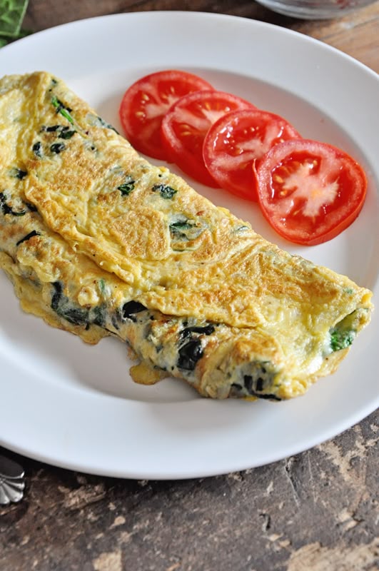 Delicious spinach omelette with sliced tomatoes on a white plate for a healthy breakfast.