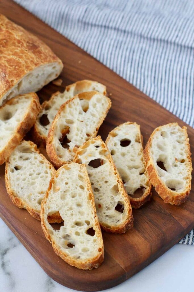 Sliced fresh sourdough bread on a wooden cutting board, showcasing airy texture and golden crust.
