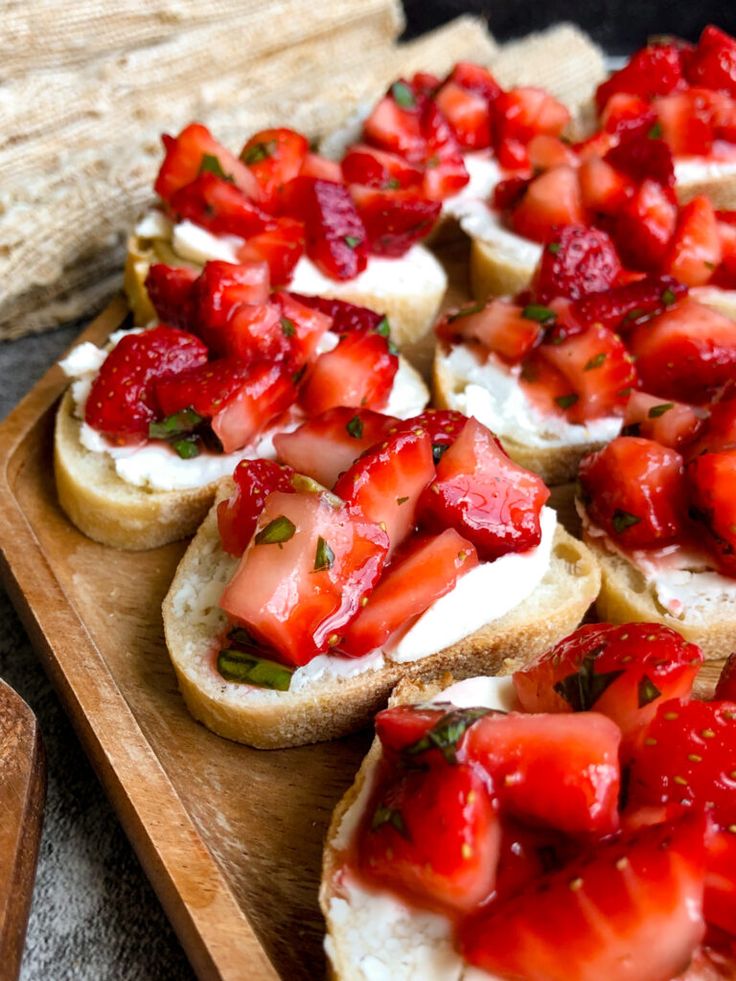 Strawberry and cream cheese bruschetta on rustic bread served on a wooden platter, garnished with fresh herbs.