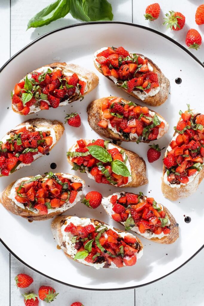 Plate of fresh strawberry bruschetta with basil and cream cheese on toasted bread slices.