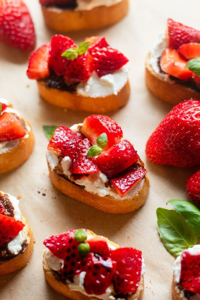 Strawberry bruschetta with ricotta on toasted bread garnished with fresh basil leaves, perfect summer appetizer.
