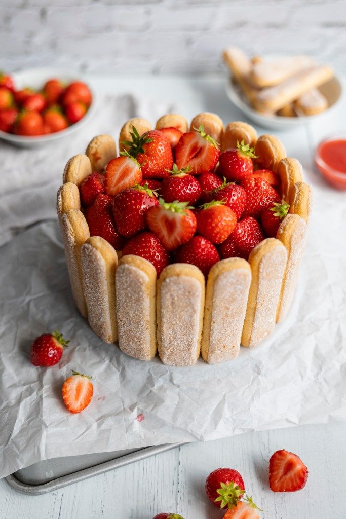 Strawberry charlotte cake with ladyfingers, topped with fresh strawberries on parchment paper.