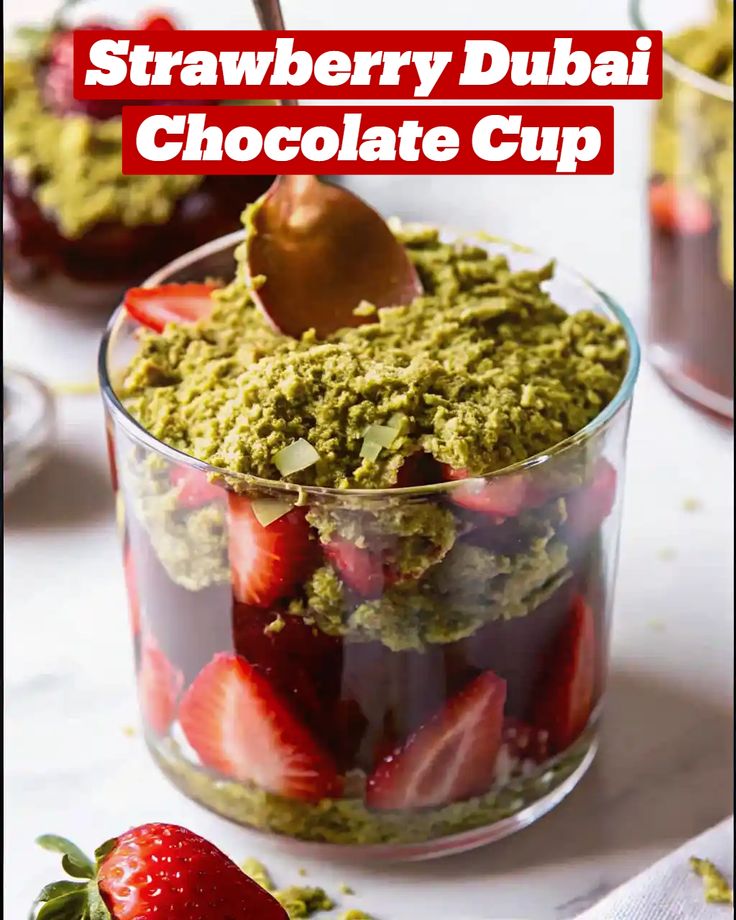 Glass cup with strawberries and green topping labeled Strawberry Dubai Chocolate Cup, with a spoon inside.