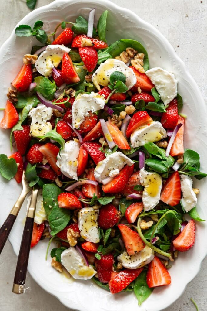 Fresh strawberry salad with creamy cheese, walnuts, and spinach on a plate, drizzled with olive oil.