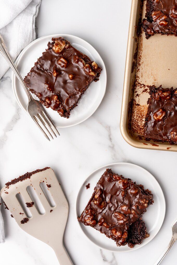 Chocolate walnut brownies on plates and baking tray with spatula and fork on a marble surface.
