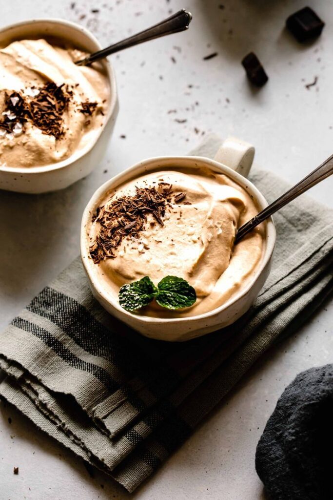 Creamy coffee mousse topped with chocolate shavings and mint in a white bowl on a cloth napkin.