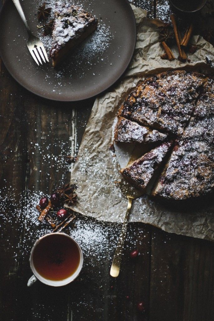 Homemade berry cake dusted with powdered sugar, served with a cup of tea on a rustic table setting.