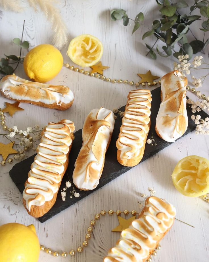 Toasted lemon meringue eclairs on a slate with fresh lemons and decorative greenery.