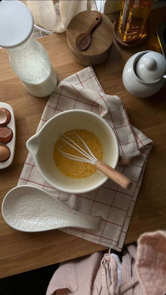 Kitchen counter with a bowl of whisked eggs, utensils, and ingredients. Suitable for baking or cooking prep.