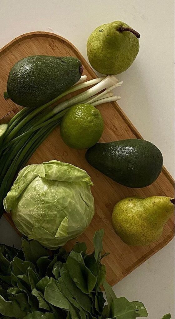 Fresh green vegetables and fruits on a wooden board: avocado, pear, cabbage, lime, and scallions.