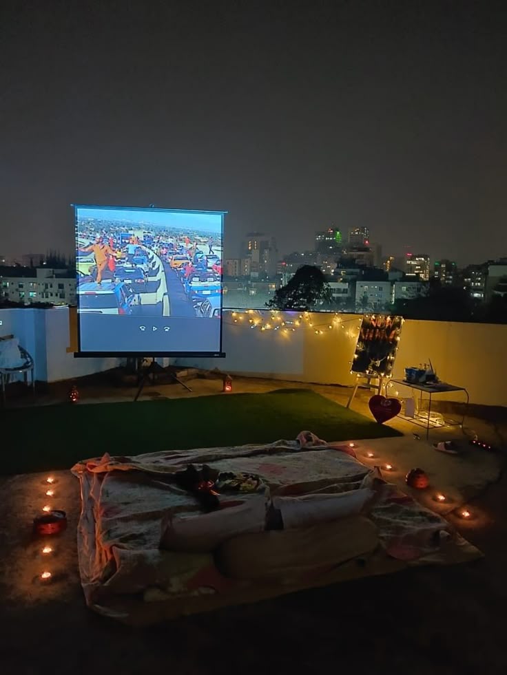 Cozy rooftop movie night setup with projector, cushions, and city skyline at night.