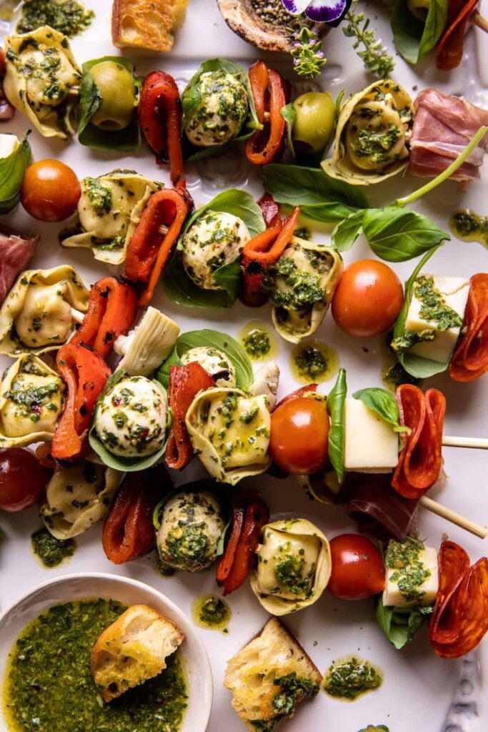 Vibrant antipasto skewers with tortellini, cherry tomatoes, olives, and pesto on a platter.