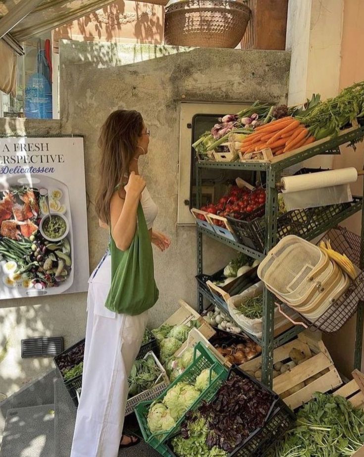 Woman shopping for fresh vegetables at an outdoor market stand with a green tote bag.