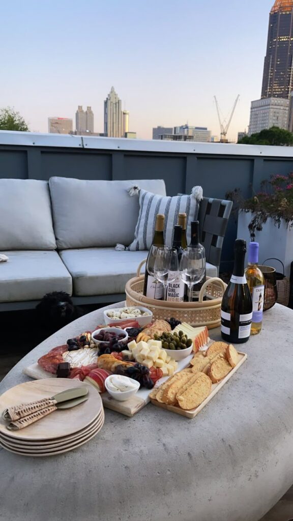 Rooftop charcuterie board with wine, cheese, and crackers, overlooking a city skyline at sunset.