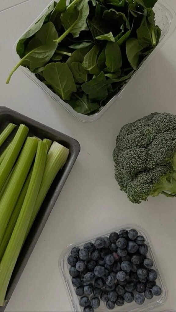Fresh spinach, celery, broccoli, and blueberries arranged on a white surface for a healthy diet.