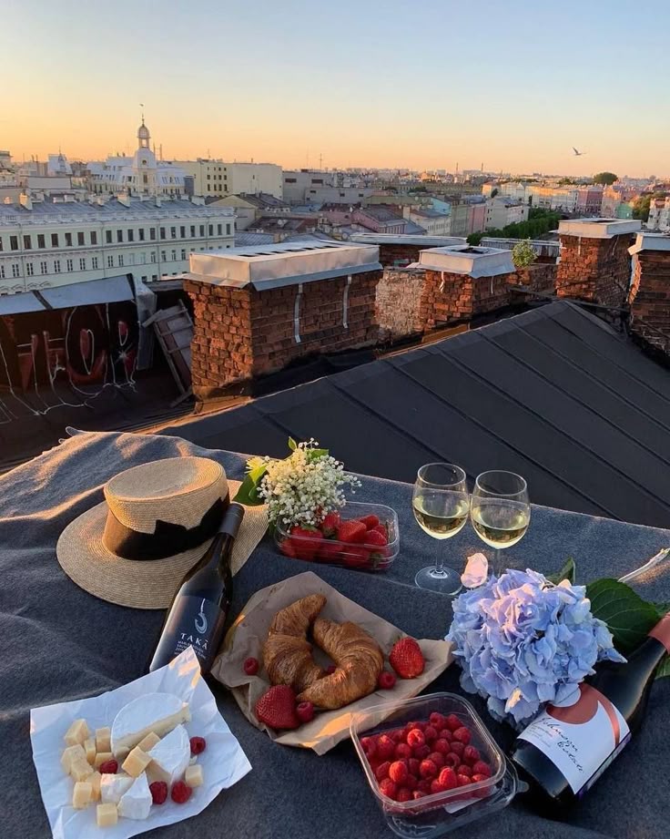Rooftop picnic with wine, croissants, berries, and cheese at sunset overlooking a cityscape.
