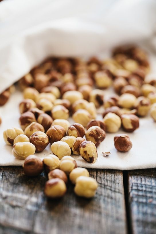 Roasted hazelnuts scattered on a rustic wooden table with a white cloth backdrop.