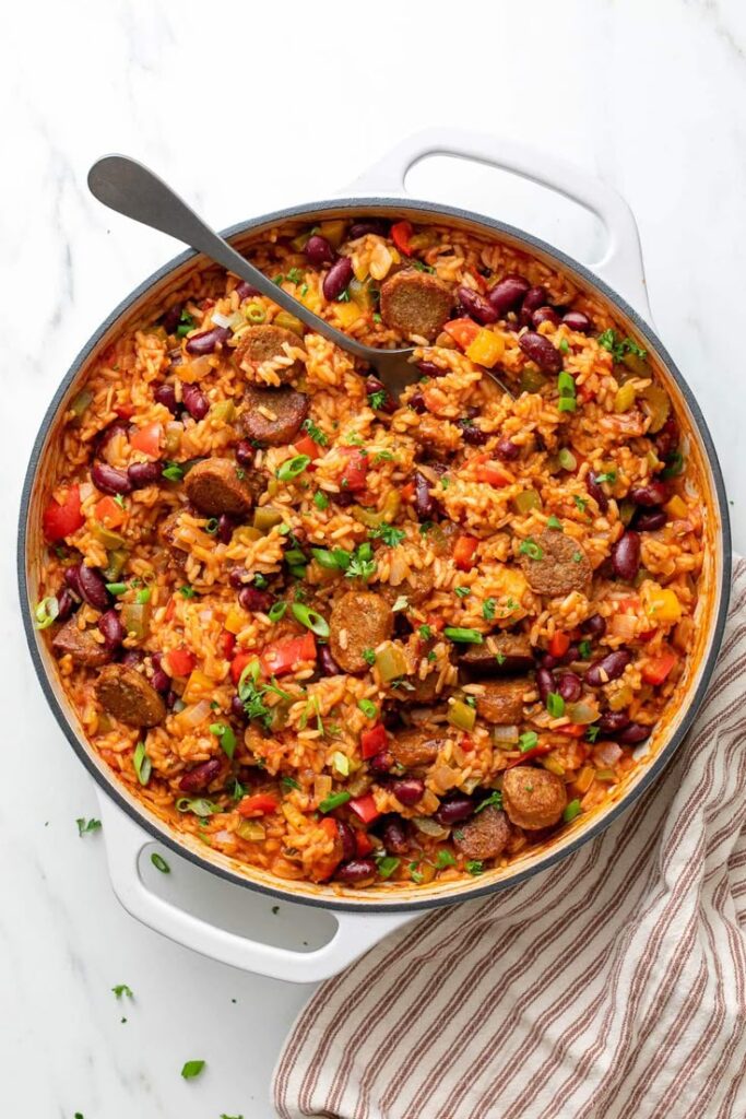 A delicious Cajun jambalaya with sausage, rice, beans, and vegetables in a large pot, garnished with fresh herbs.