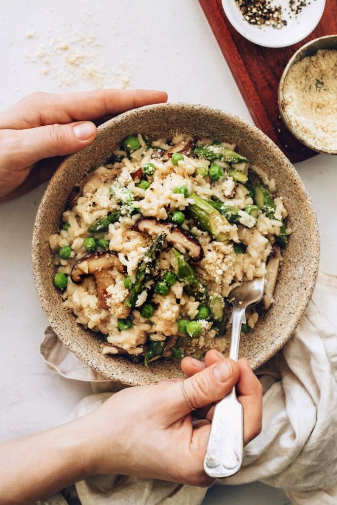 Delicious creamy mushroom risotto with peas and asparagus in a rustic bowl, garnished with grated cheese and spices.