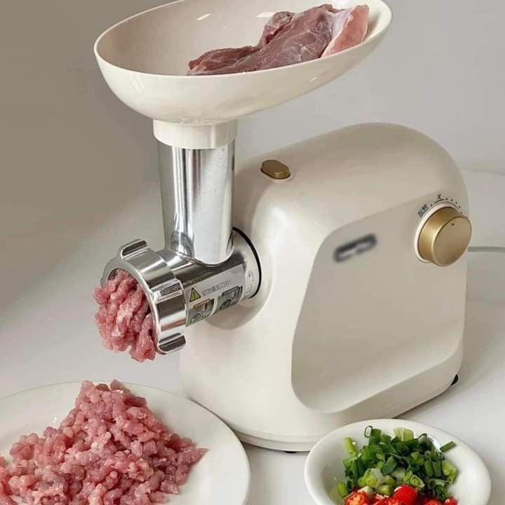 Electric meat grinder processing fresh meat into minced meat on a kitchen counter.