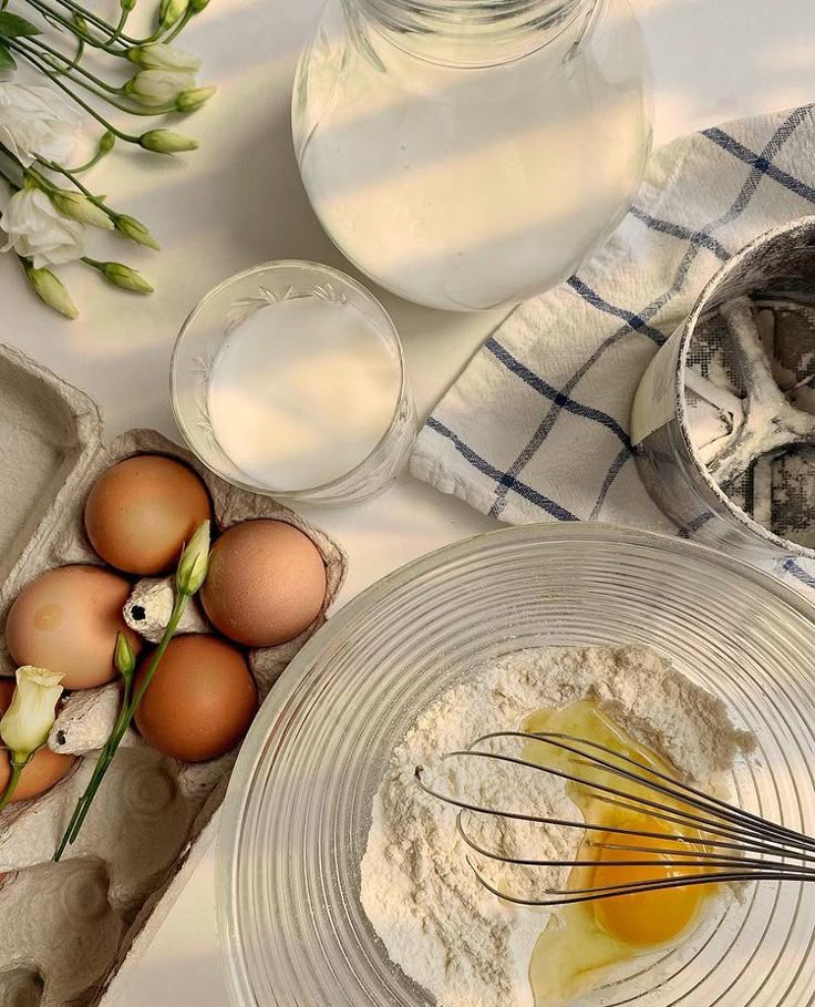 Baking ingredients on a table: flour, eggs, milk, and whisk in a bowl; fresh, rustic kitchen setup.
