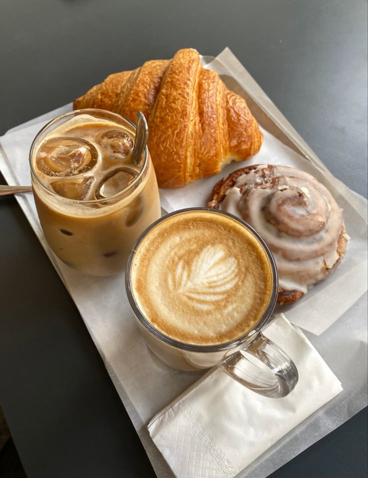 Coffee latte art and iced coffee with a croissant and cinnamon roll on a tray. Perfect breakfast setting.