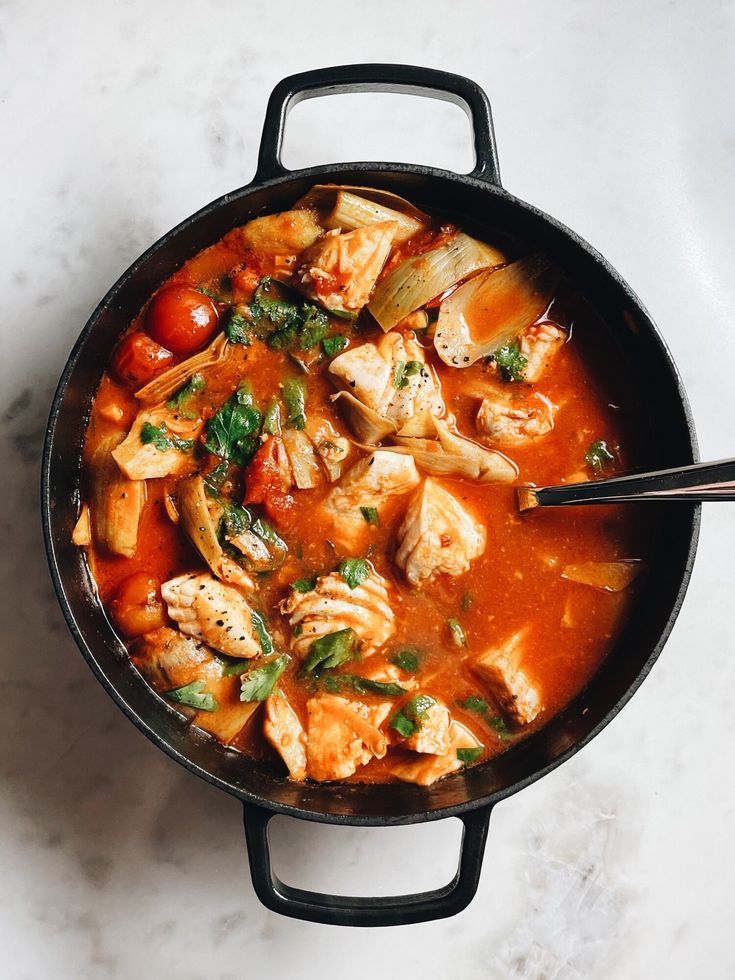 Hearty fish stew with tomatoes and herbs in a black pot, a comforting and flavorful seafood dish perfect for dinner.