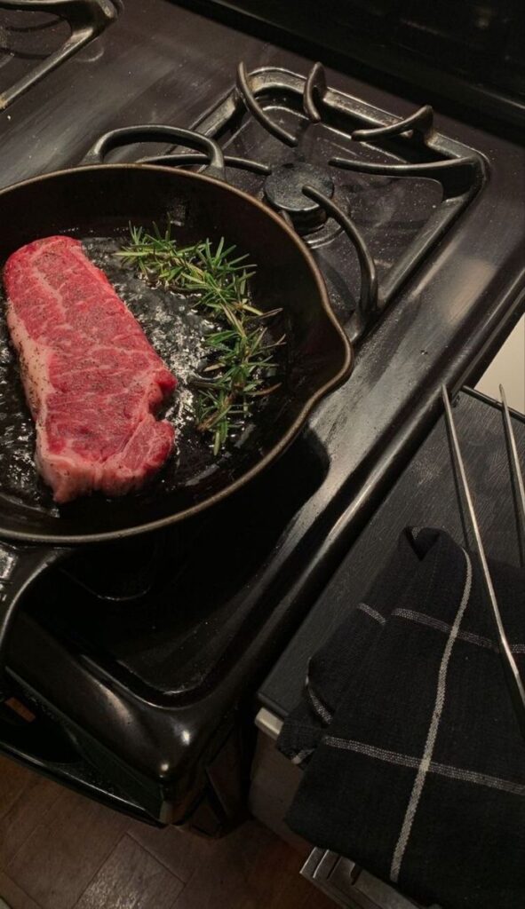 Steak with rosemary sizzling in a cast iron skillet on a stove.