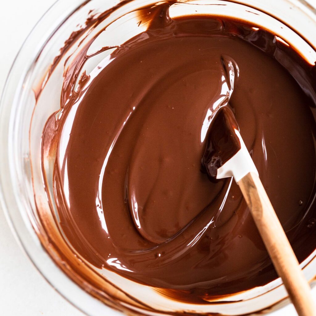 Smooth melted chocolate in a glass bowl with a spatula, perfect for baking or dessert recipes.