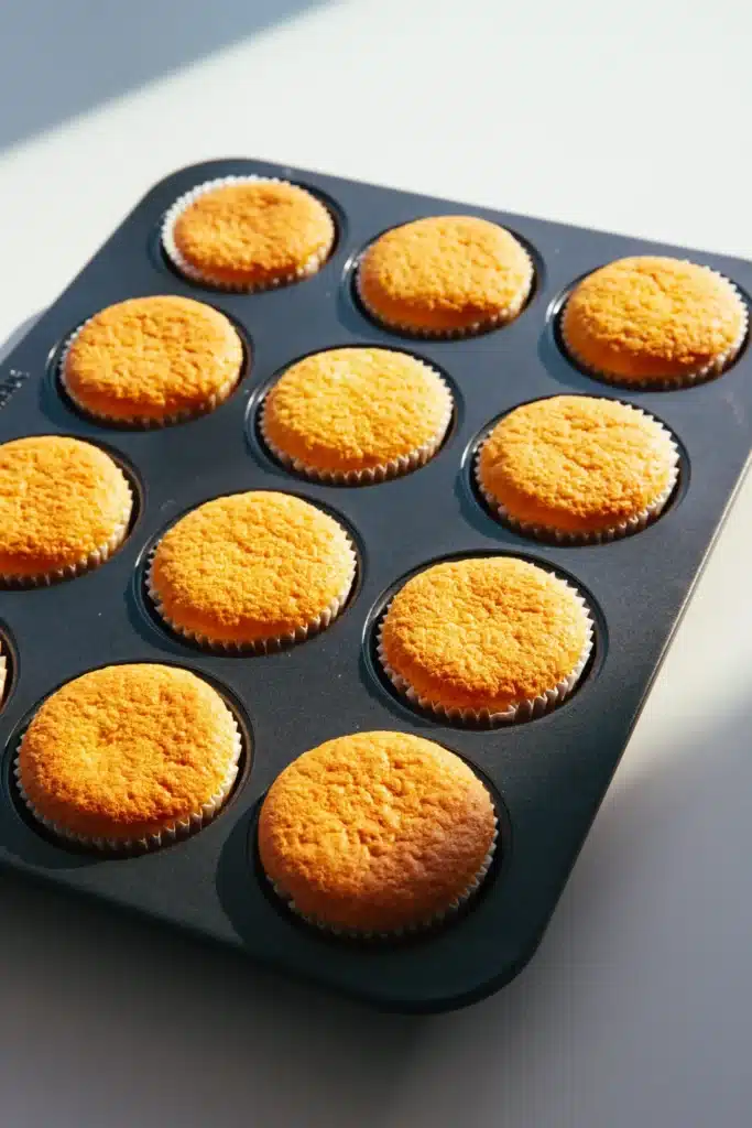 Freshly baked cupcakes in a muffin tray with golden brown tops, bathed in sunlight.