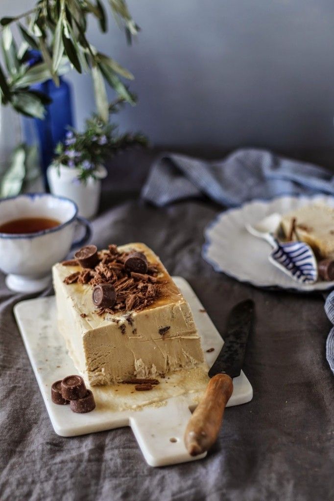 Delicious ice cream cake topped with chocolate pieces on a marble board beside tea, capturing a cozy dessert moment.