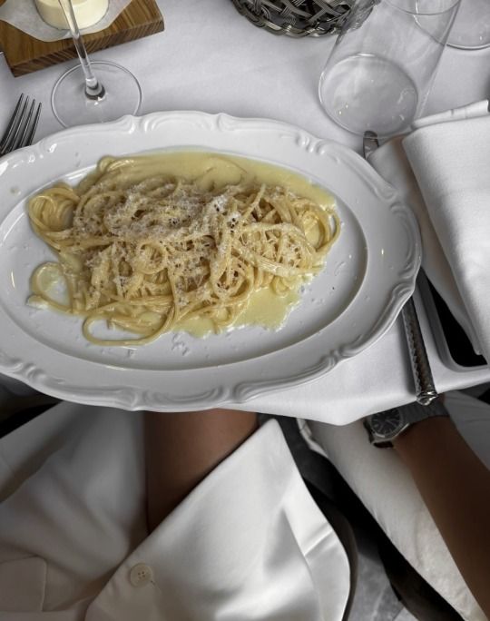 Plate of spaghetti with creamy cheese sauce on a white table setting, viewed from above.