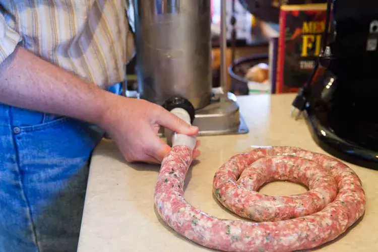 Person making homemade sausage with stuffing machine on kitchen counter.