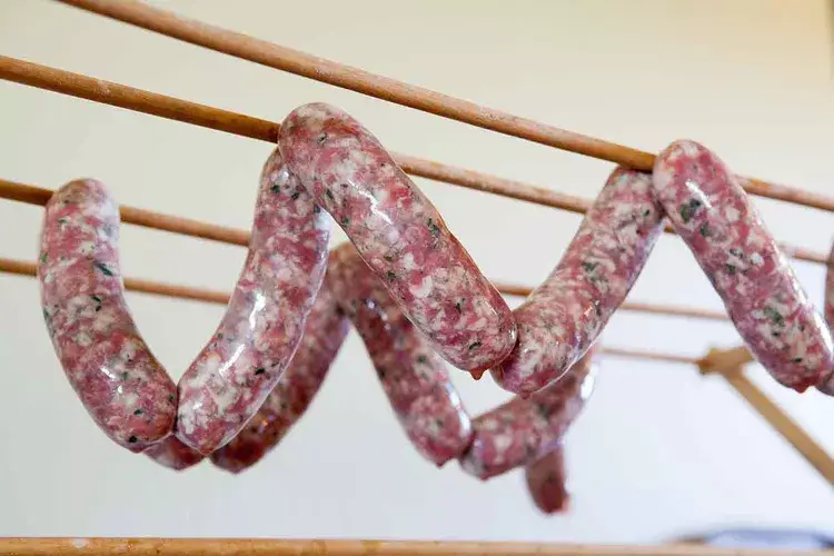 Fresh sausages hanging on wooden rods, ready to dry, showcasing homemade cured meats and traditional preservation.