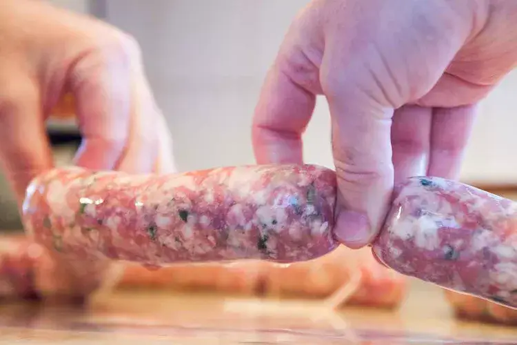 Hands crafting homemade sausages, showing close-up of raw meat mixture encased in natural casing.