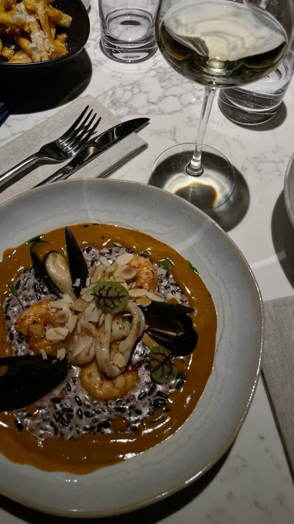 Seafood risotto with shrimp and mussels, served with a glass of white wine on a marble table.