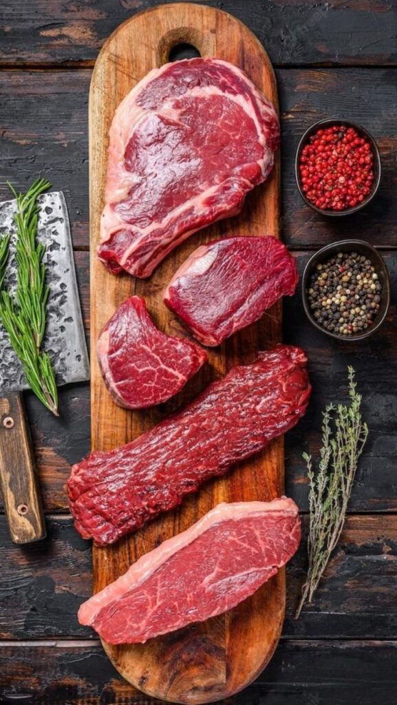 Assorted raw beef cuts on a wooden board with herbs and spices, ideal for grilling or cooking.