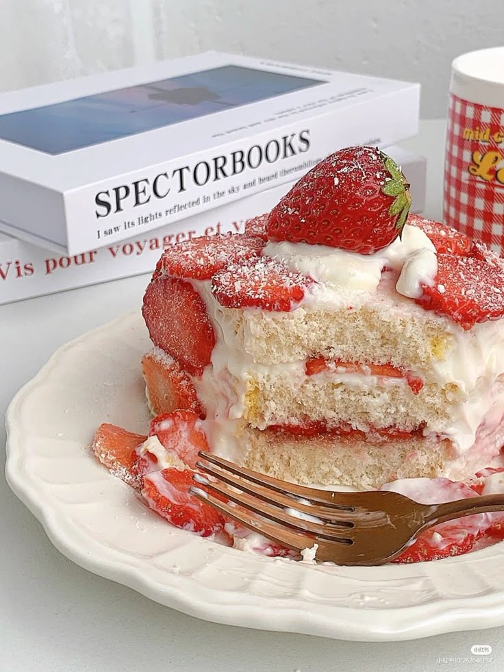 Strawberry shortcake with cream on a white plate, surrounded by books for a cozy dessert setting.