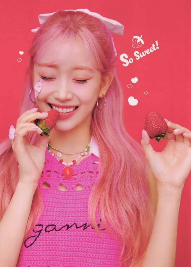 Smiling person with pink hair holding strawberries, wearing pink crochet top. Text reads So Sweet! with heart graphics.