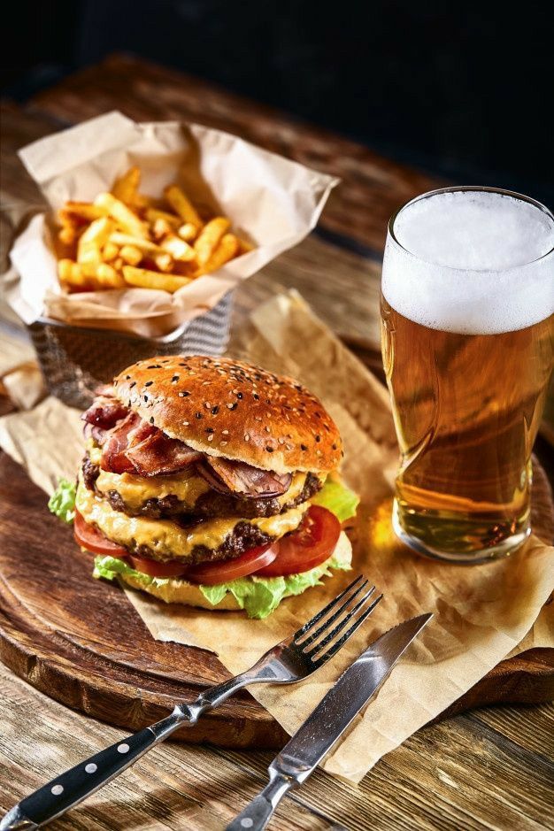 Delicious cheeseburger with bacon, crispy fries, and cold beer on a wooden table for a perfect meal.