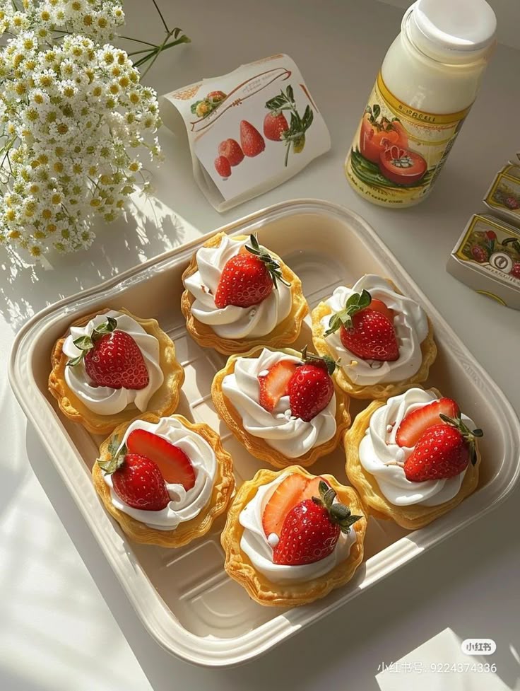 Strawberry cream tarts in a tray with whipped cream and fresh strawberries, bottle and flowers nearby.